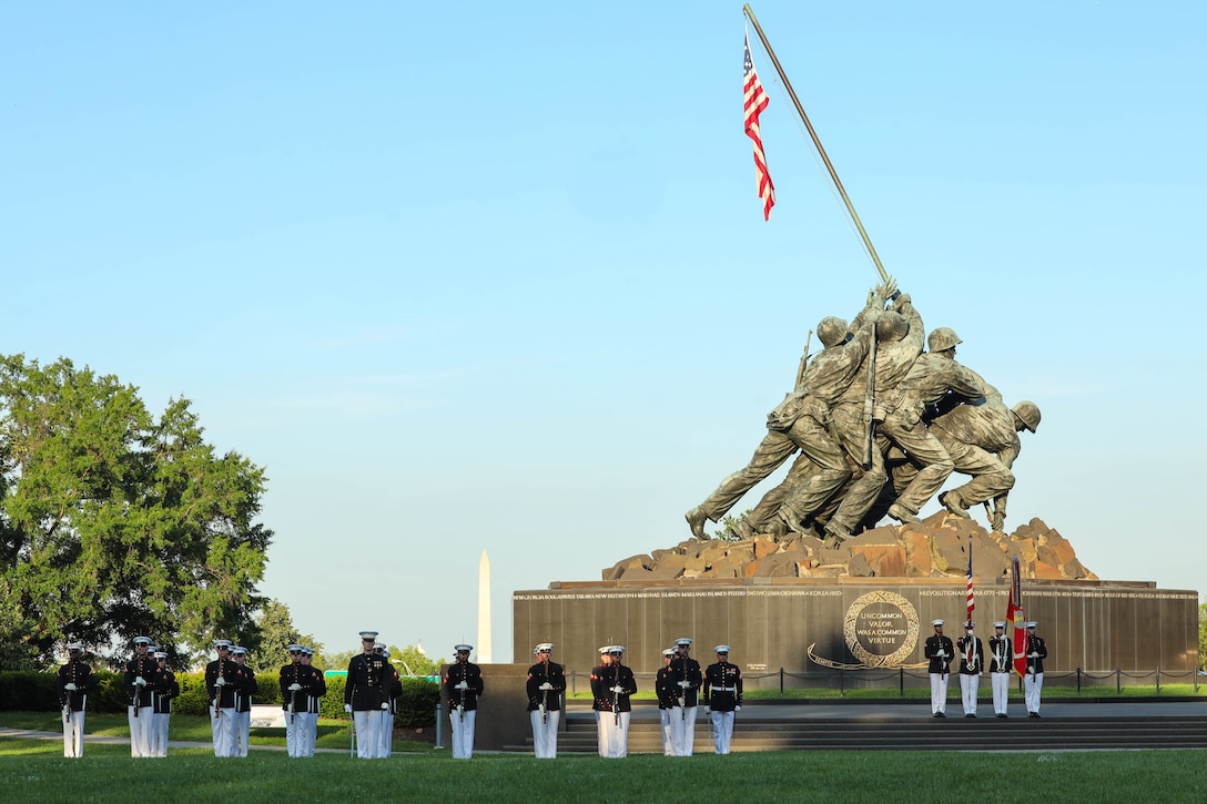 Marines stand in formation in front of a memorial statue outside.