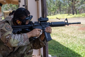 A U.S. Air Force Airmen fires an M4 carbine rifle at practice targets while wearing a gas mask during combat arms training and maintenance.