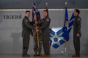4 men stand on stage, one of which are handing a guidon to another.