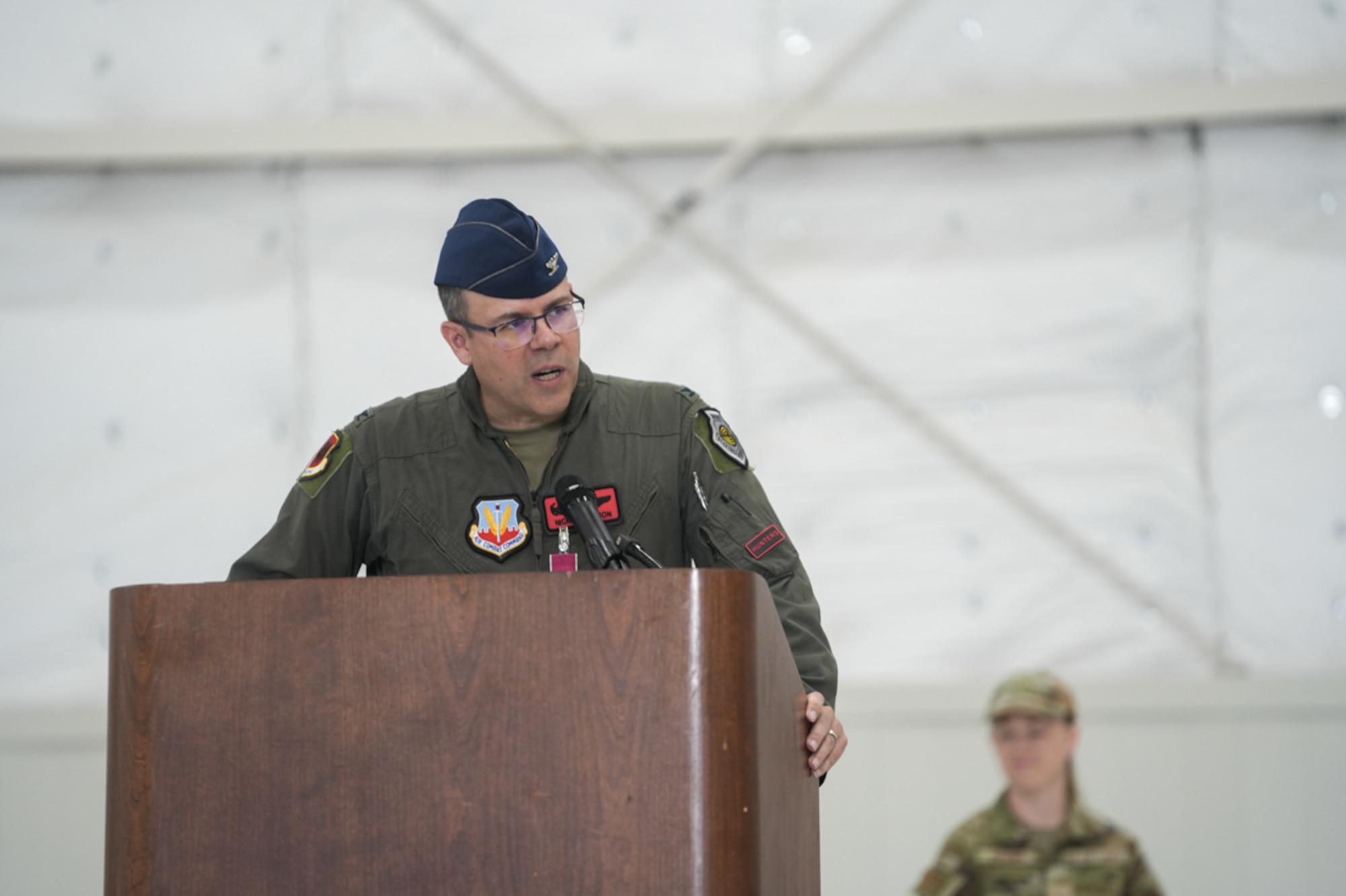 A man in a flight suit speaks at a podium.