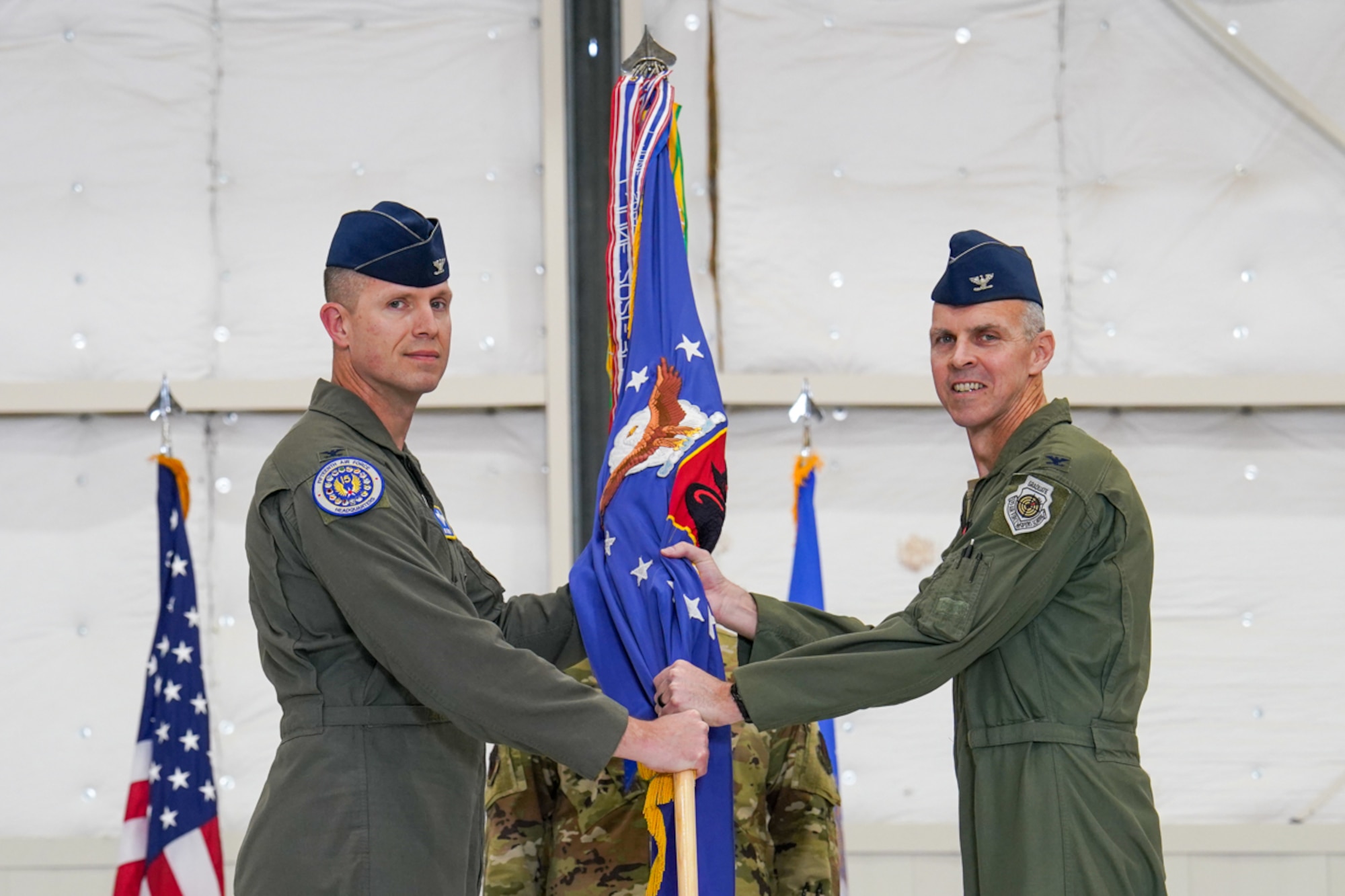 A man in a flight suit hands a guidon to another man in a flight suit.