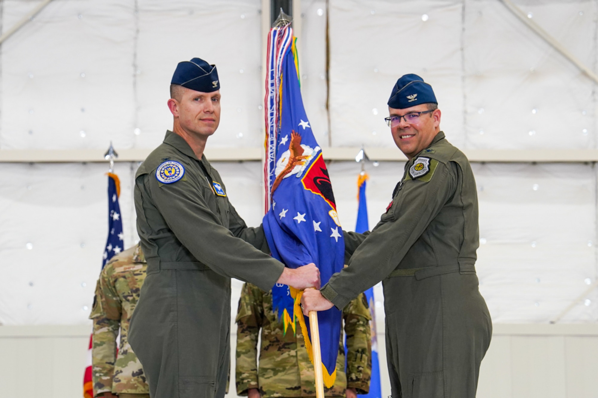 A man in a flight suit hands a guidon to a man in a flight suit.