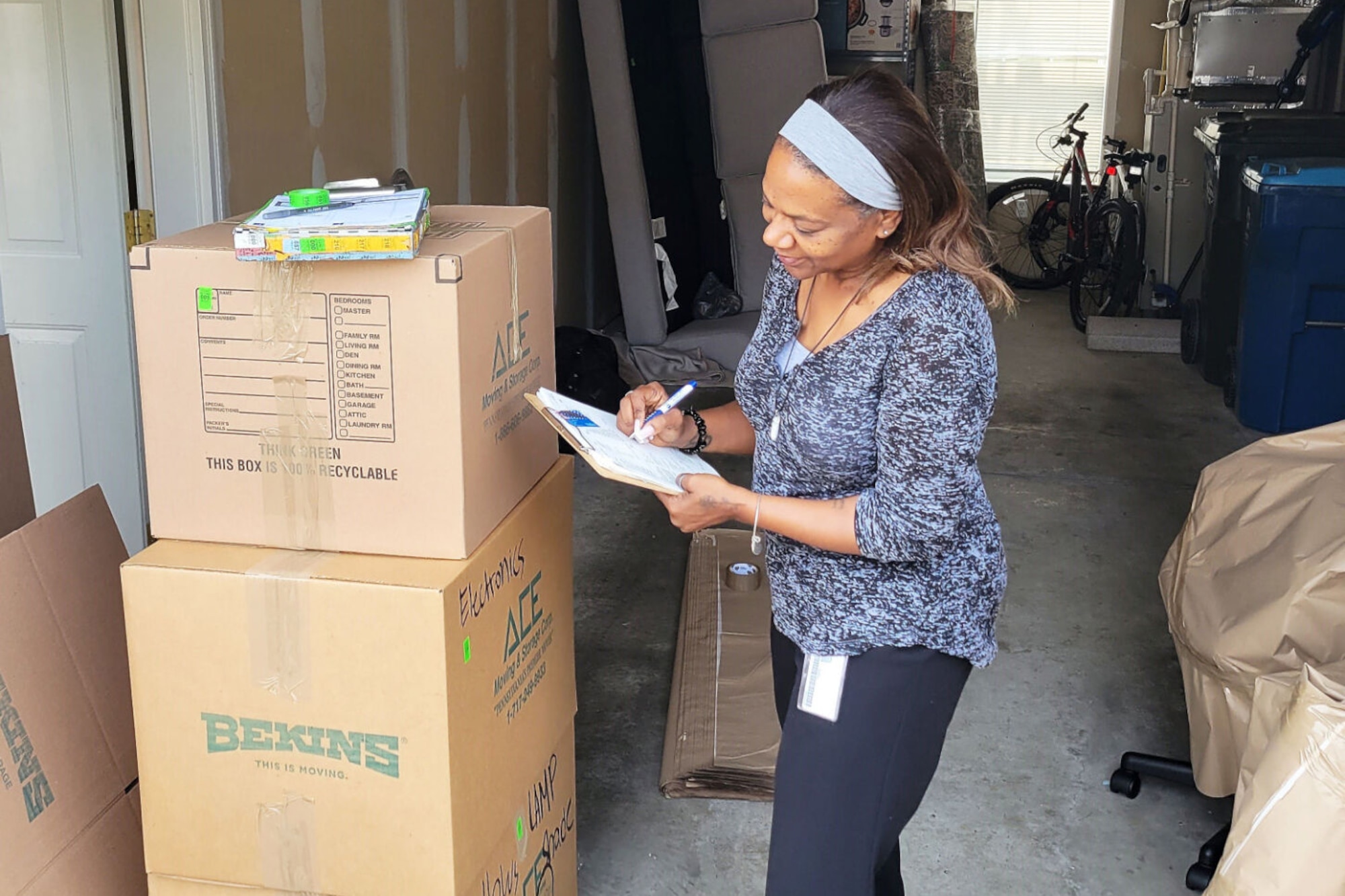A woman with a clipboard stands next to three large cardboard boxes and checks items on a list.