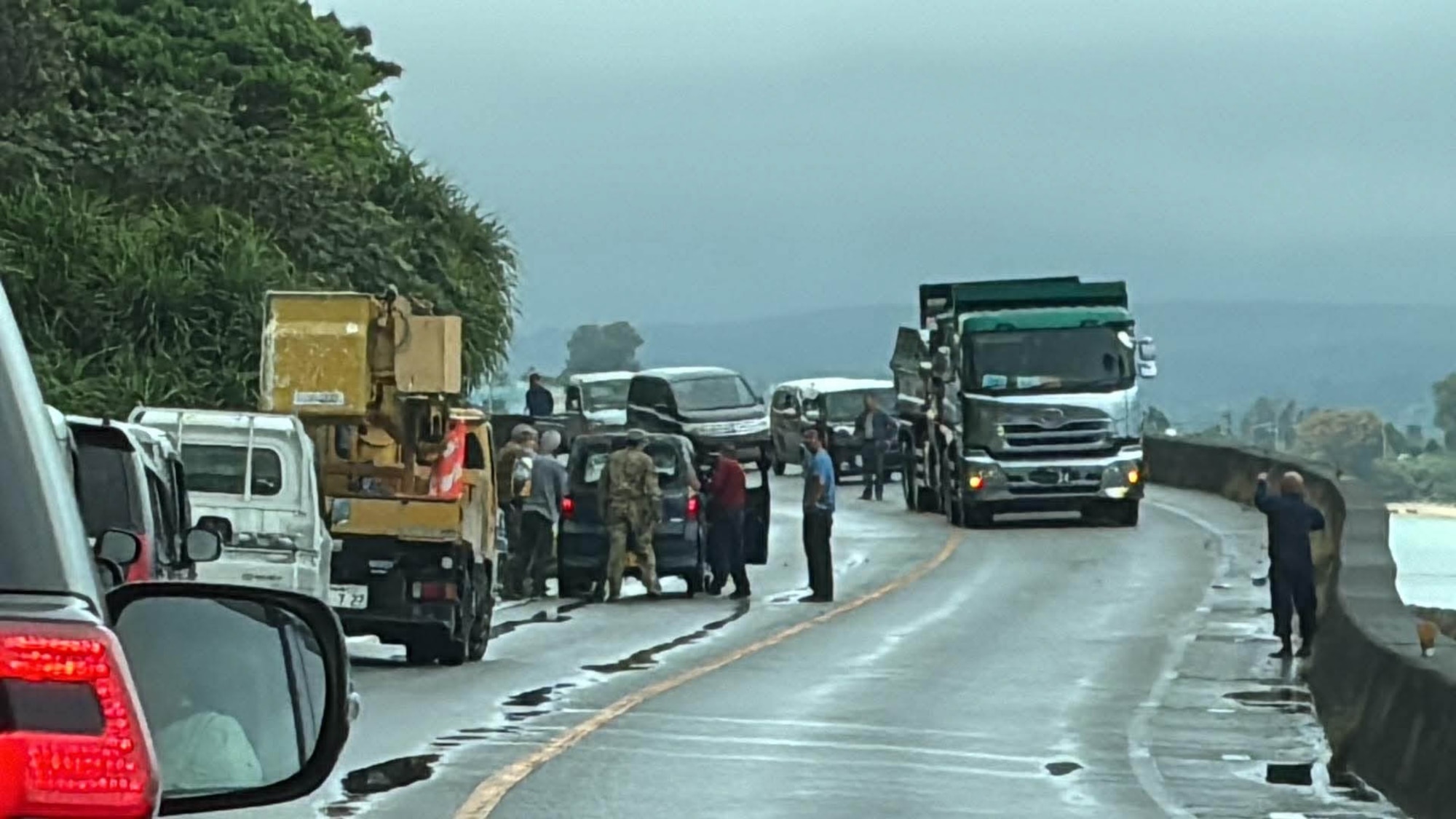 Service members and Okinawan locals help move car off road.