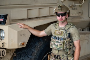 Service member poses in front of a vehicle.