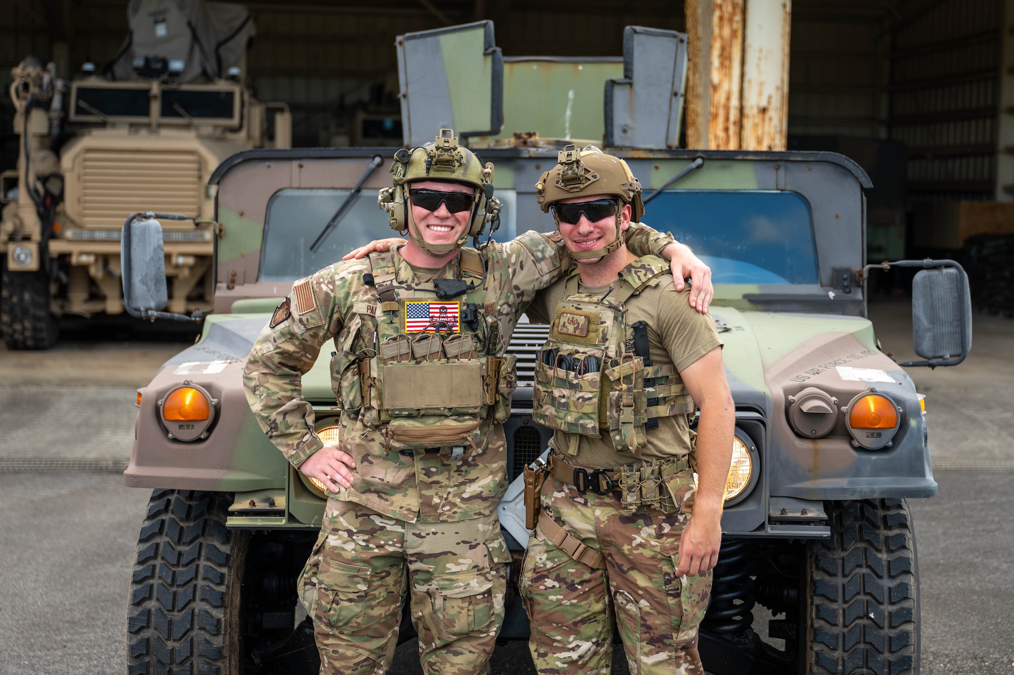 Two service members stand in front of vehicle and pose for a photo.