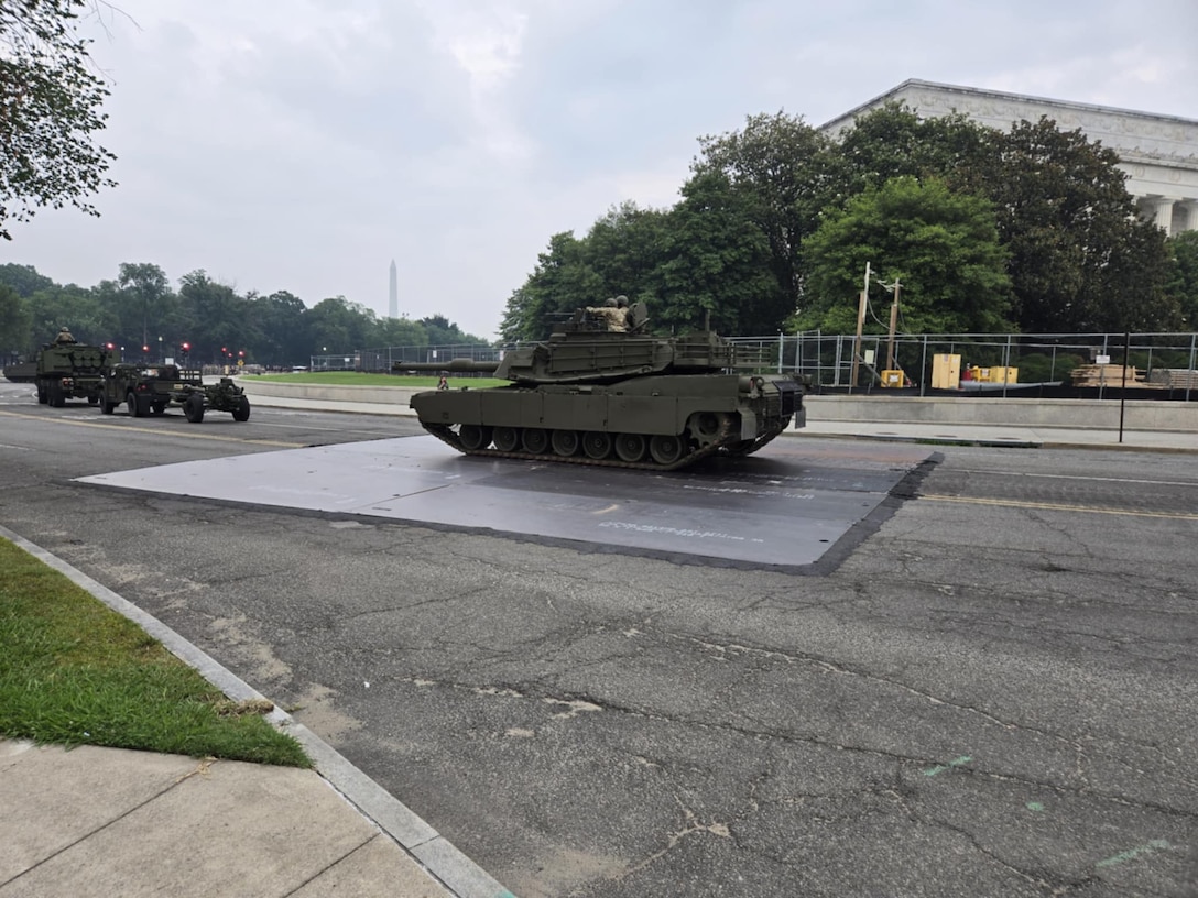 A tank rests on top of a large steel plate in the middle of a roadway.