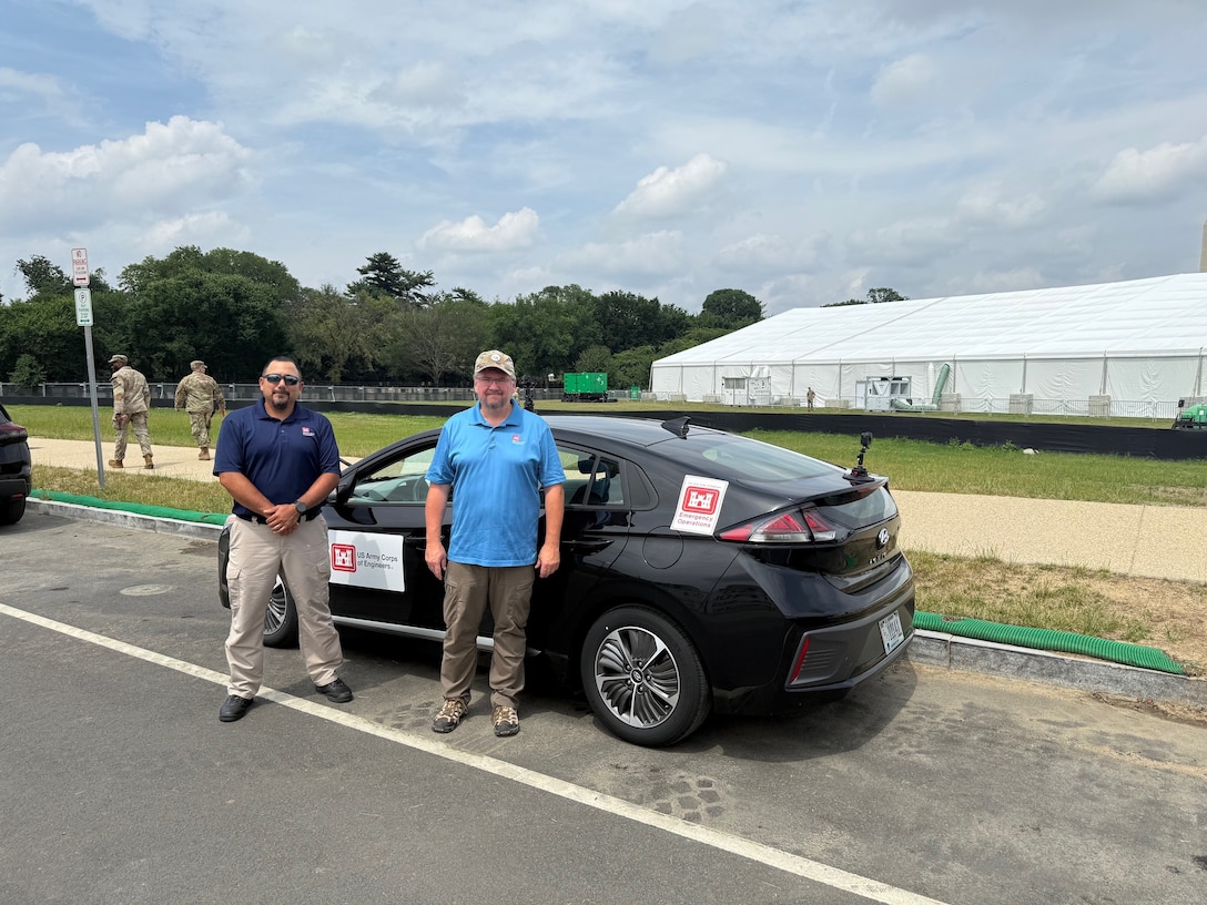 Two men stand in front of a small black car with U.S. Army Corps of Engineers placards on the side. The car has special cameras and antennas attached to it.