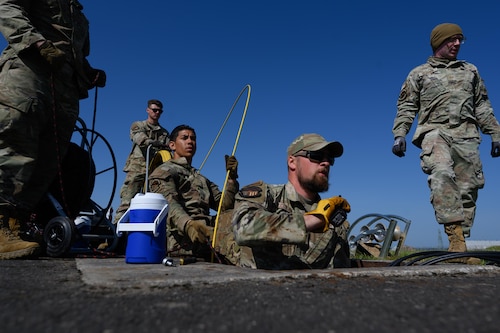 A group of people pull wiring and rope from a manhole in the ground.