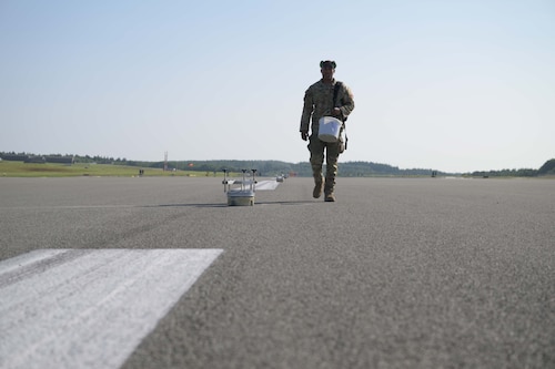 A person carrying a bucket walk along the runway centerline past fixtures being replaced.