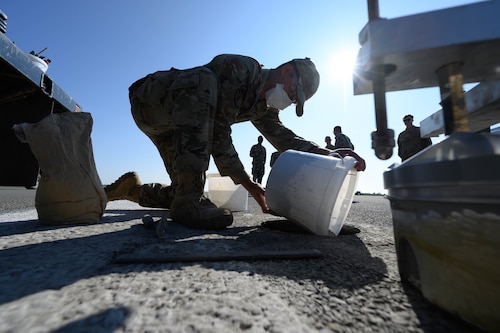 A person pours concrete mix into a hole in the runway.