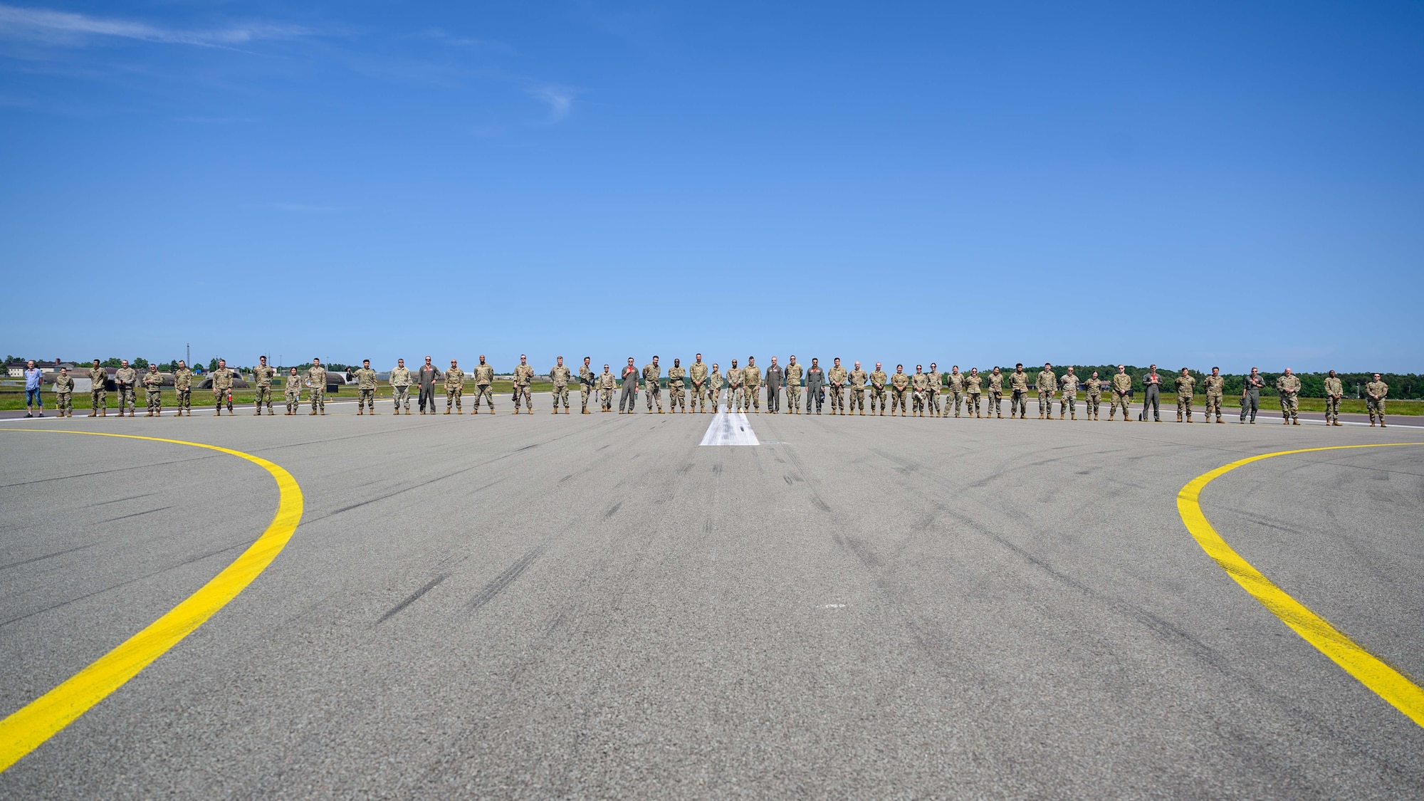 A row of Airmen stand across the width of a flightline.