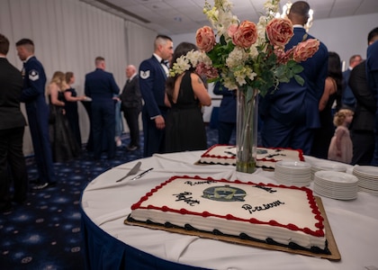 photo of a cake on a table in the foreground and Air Force Honor Guard members and family socializing in the background