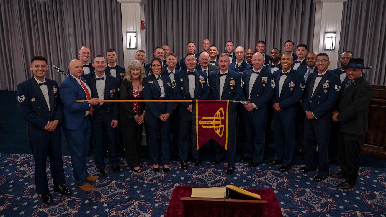 group photo of former and current Air Force Honor Guard members while one holds a guidon horizontally across the group