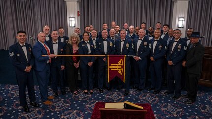 group photo of former and current Air Force Honor Guard members while one holds a guidon horizontally across the group
