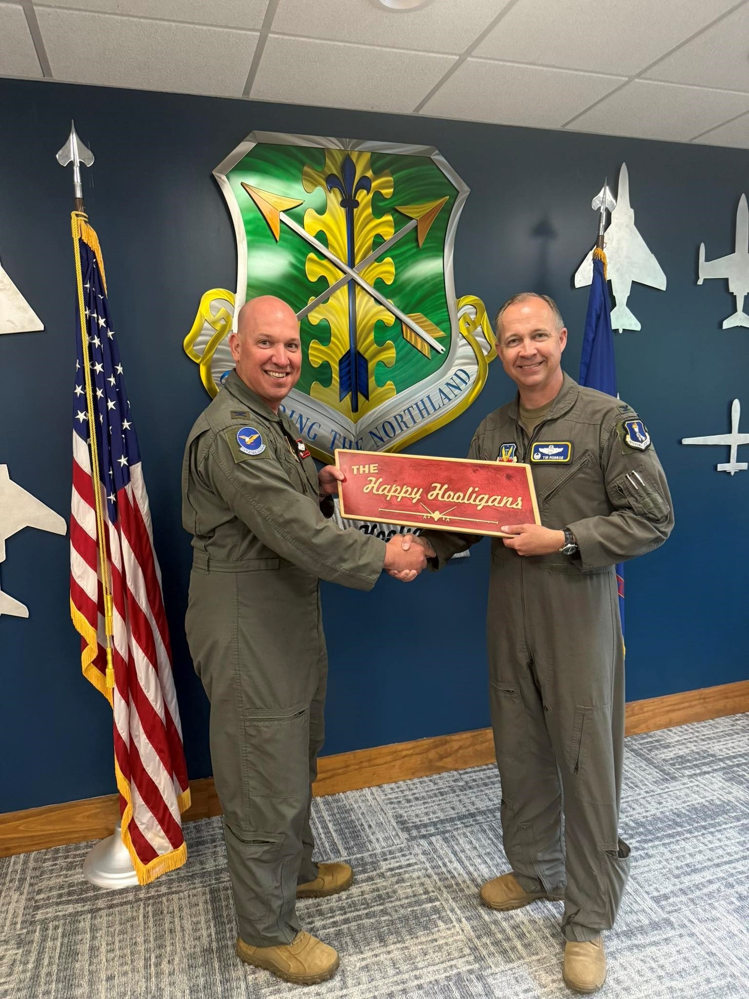 Two men in flight suits hold a red plaque