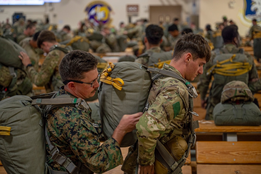U.S. Marine Corps Cpl. Robert Furton, left, 4th Air Naval Gunfire Liaison Company joint fires observer, inspects the parachute of U.S. Army Spc. Jarron Kurth, Headquarters and Headquarters Company, 2nd Infantry Brigade Combat Team, 11th Airborne Division, before a static line jump from a C-130 Hercules during Red Flag-Alaska 25-2 at Joint Base Elmendorf-Richardson, Alaska, June 25, 2025. This exercise simulates the complexities of potential Indo-Pacific scenarios, providing unique opportunities to integrate various forces into joint, coalition and multilateral training from simulated forward operating bases, enhancing the U.S. and allies’ ability to respond effectively to contingencies in the region. (U.S. Air Force photo by Senior Airman Matthew Arachikavitz)