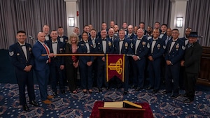 group photo of former and current Air Force Honor Guard members while one holds a guidon horizontally across the group