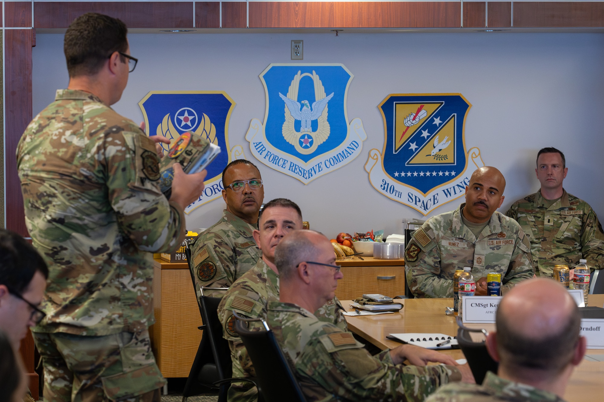 An individual in military uniform standing up and speaking to a group of individuals seated at a table.