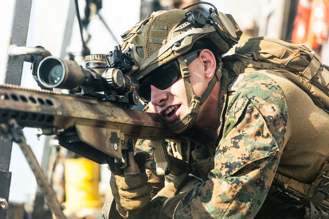 A close-up of a Marine in tactical gear looking through the scope of a weapon.