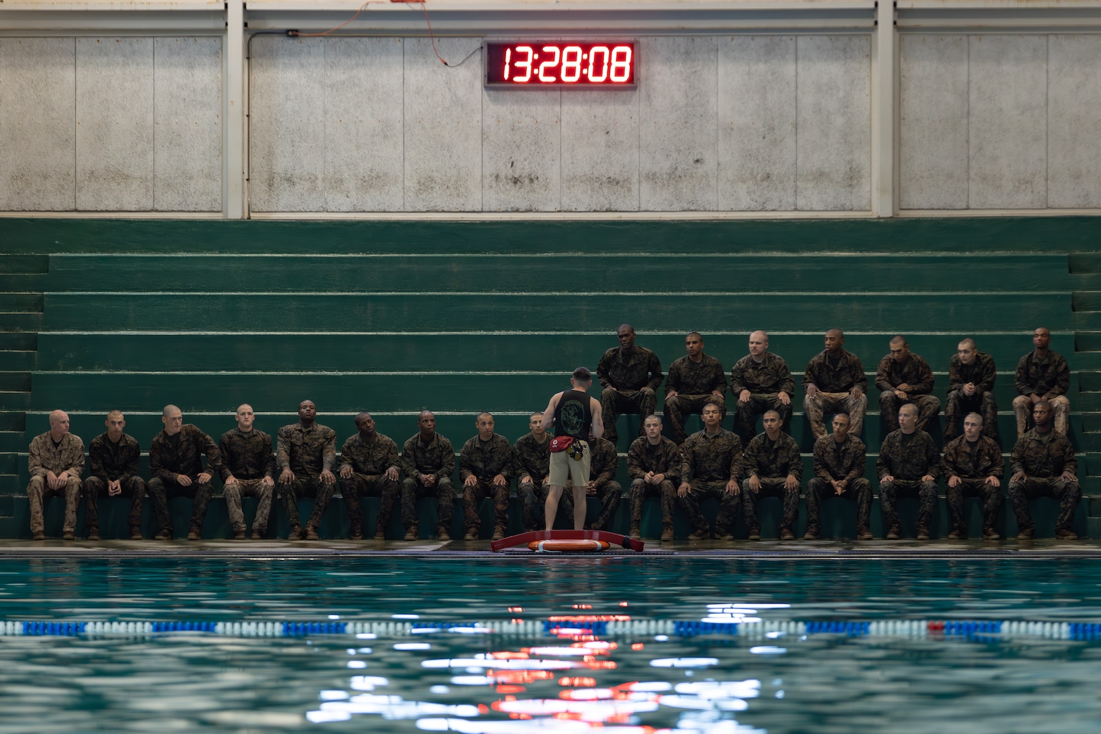 Water survival instructor gives recruits sitting on bleachers on the pool deck knowledge on how to stay afloat for their swim qualifications test.
