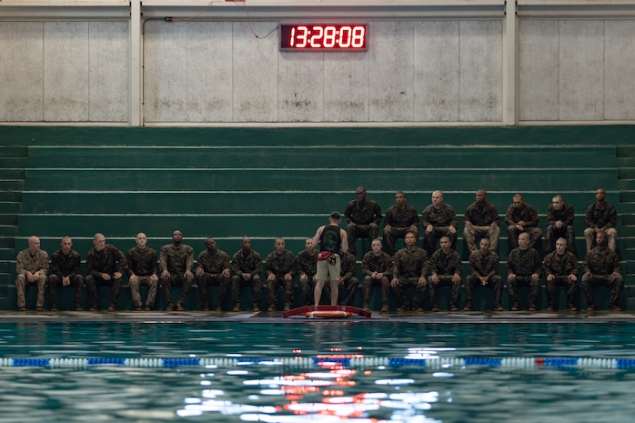 Water survival instructor gives recruits sitting on bleachers on the pool deck knowledge on how to stay afloat for their swim qualifications test.