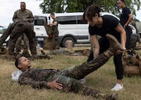 Athletic trainer stretches the leg of a Marine while he lays on his back after a hike.