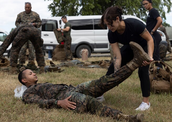 Athletic trainer stretches the leg of a Marine while he lays on his back after a hike.