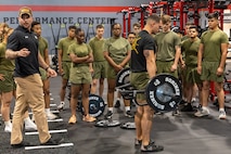 Strength instructor guides a Marinein PT gear to perform a lift technique with a hex bar.
