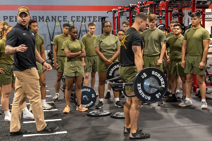 Strength instructor guides a Marinein PT gear to perform a lift technique with a hex bar.