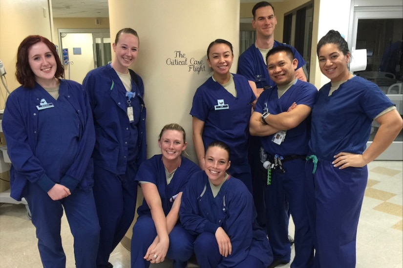 Eight people in medical attire pose for a photo in a room by a column.