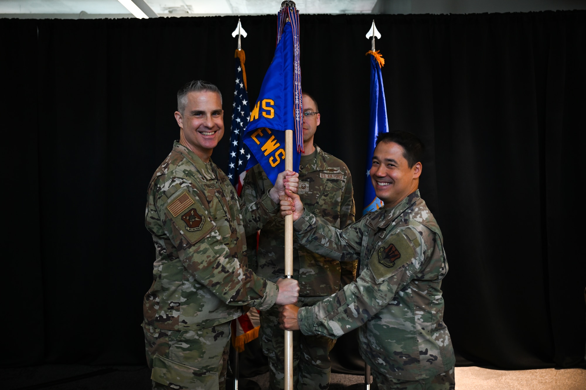 U.S. Air Force Col. Andrew Finkler, 850th Spectrum Warfare Group commander, left, passes the guidon to U.S. Air Force Lt. Col. Adrian De Freitas, 563d Electronic Warfare Squadron commander, right, during the 563 EWS change of command ceremony in San Antonio, Texas, June 26. 2025. This is the unit’s second change of command since reactivating in 2024 as a software development unit under the 350th Spectrum Warfare Wing. (U.S. Air Force photo by Capt. Benjamin Aronson)