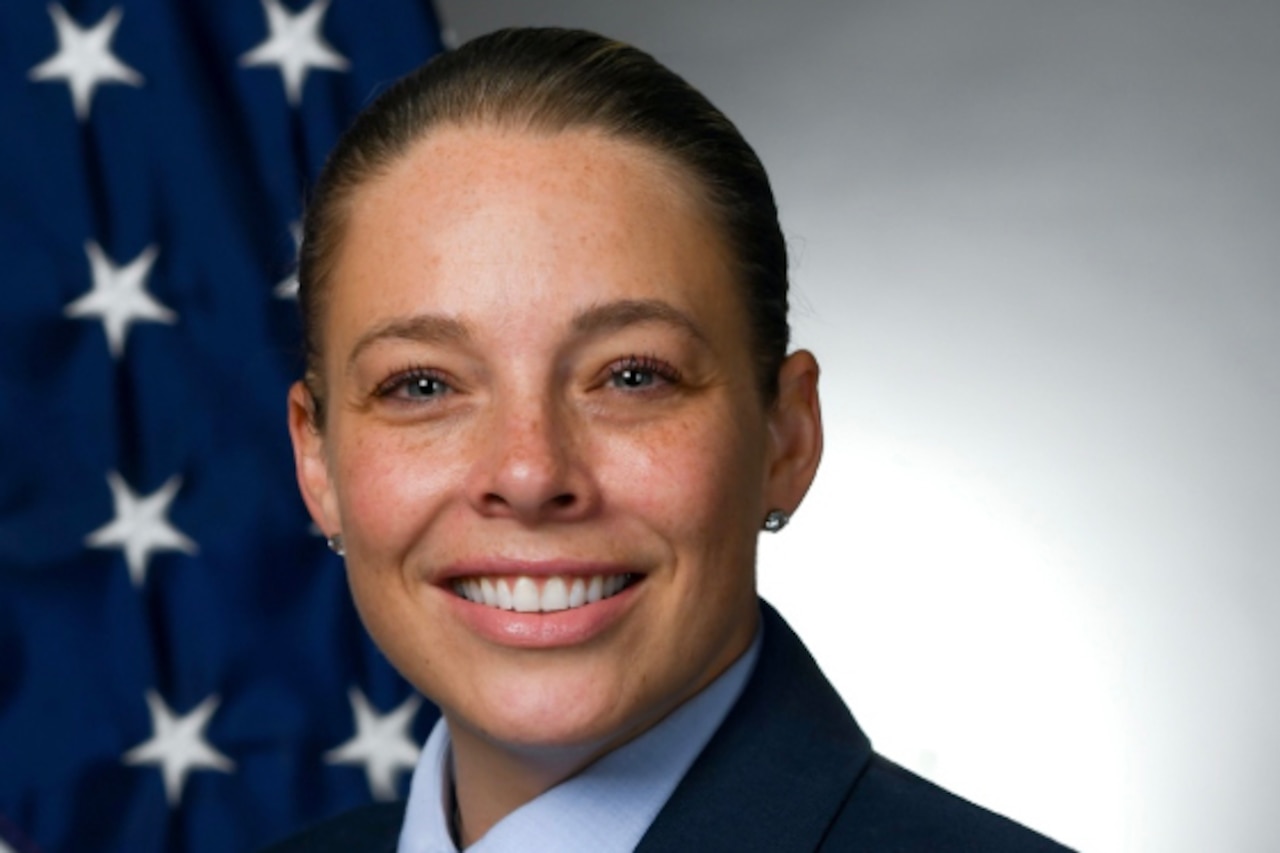 Woman in military uniform poses for an official photo next to the U.S. flag.