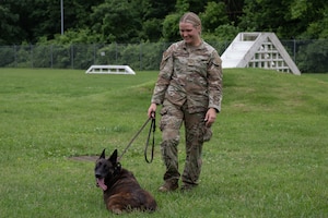 U.S. Air Force Staff Sgt. Alexis Krippel, left, smiles while speaking with Col. Jun S. Oh during a recognition visit at Joint Base Andrews, Maryland, on June 16, 2025. Both are in uniform, standing outdoors in a casual, friendly exchange. Oh recognized Krippel for her exceptional performance as a military working dog handler.