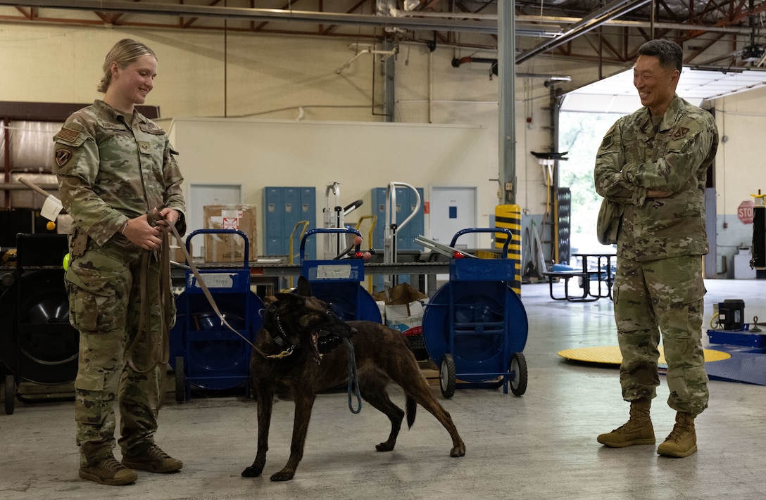 U.S. Air Force Staff Sgt. Alexis Krippel, left, smiles while speaking with Col. Jun S. Oh during a recognition visit at Joint Base Andrews, Maryland, on June 16, 2025. Both are in uniform, standing outdoors in a casual, friendly exchange. Oh recognized Krippel for her exceptional performance as a military working dog handler.