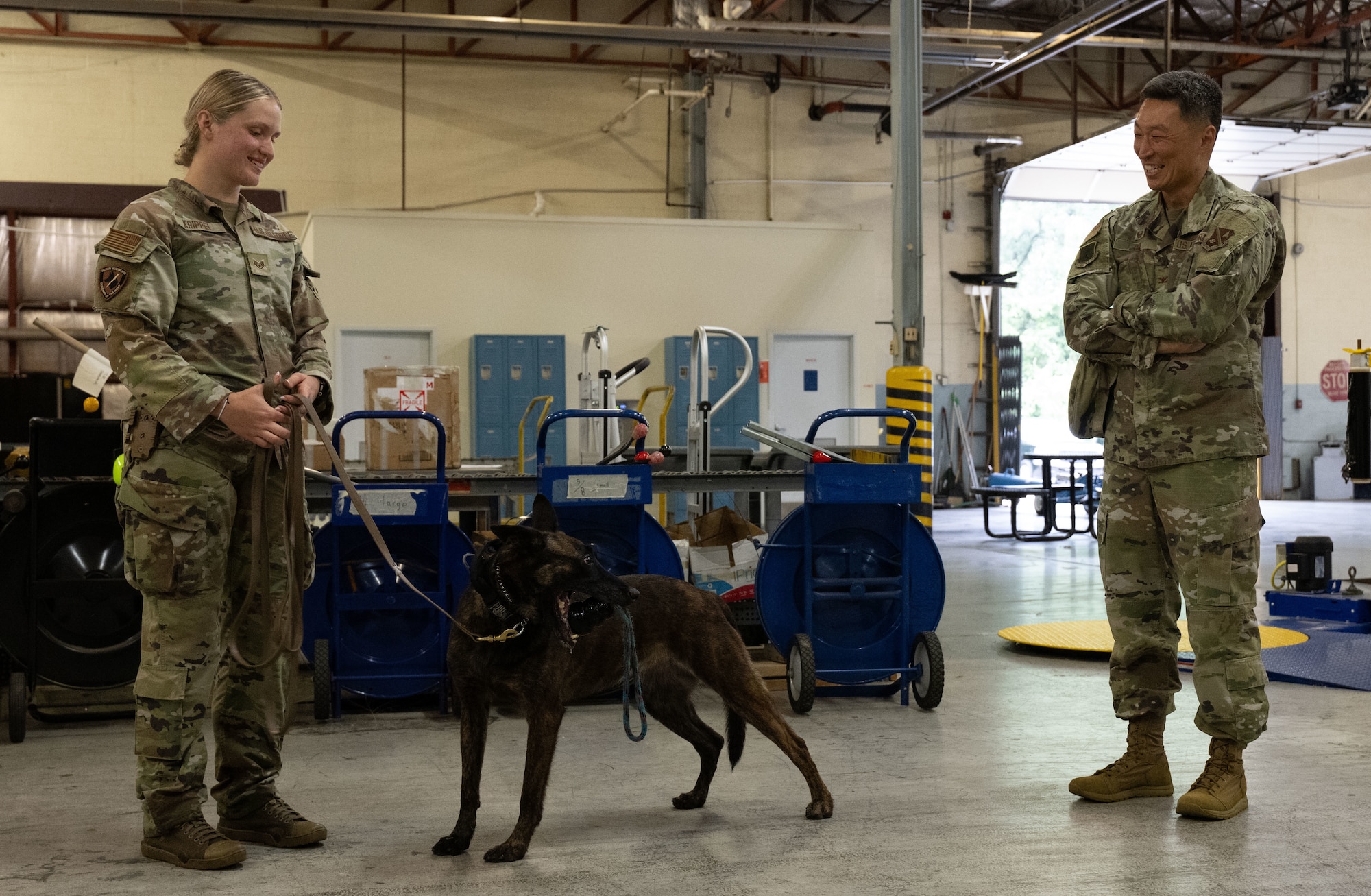 U.S. Air Force Staff Sgt. Alexis Krippel, left, smiles while speaking with Col. Jun S. Oh during a recognition visit at Joint Base Andrews, Maryland, on June 16, 2025. Both are in uniform, standing outdoors in a casual, friendly exchange. Oh recognized Krippel for her exceptional performance as a military working dog handler.