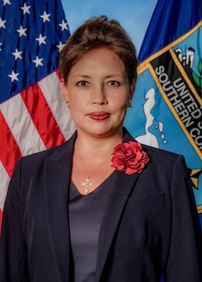 Posed photo of a woman in a dark blue suit with flags in the background