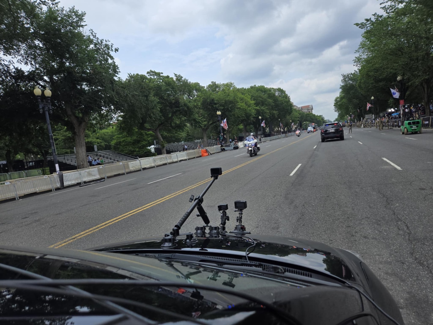The view of a  hood of a car with multiple cameras and antennas as it goes down the middle of a street.