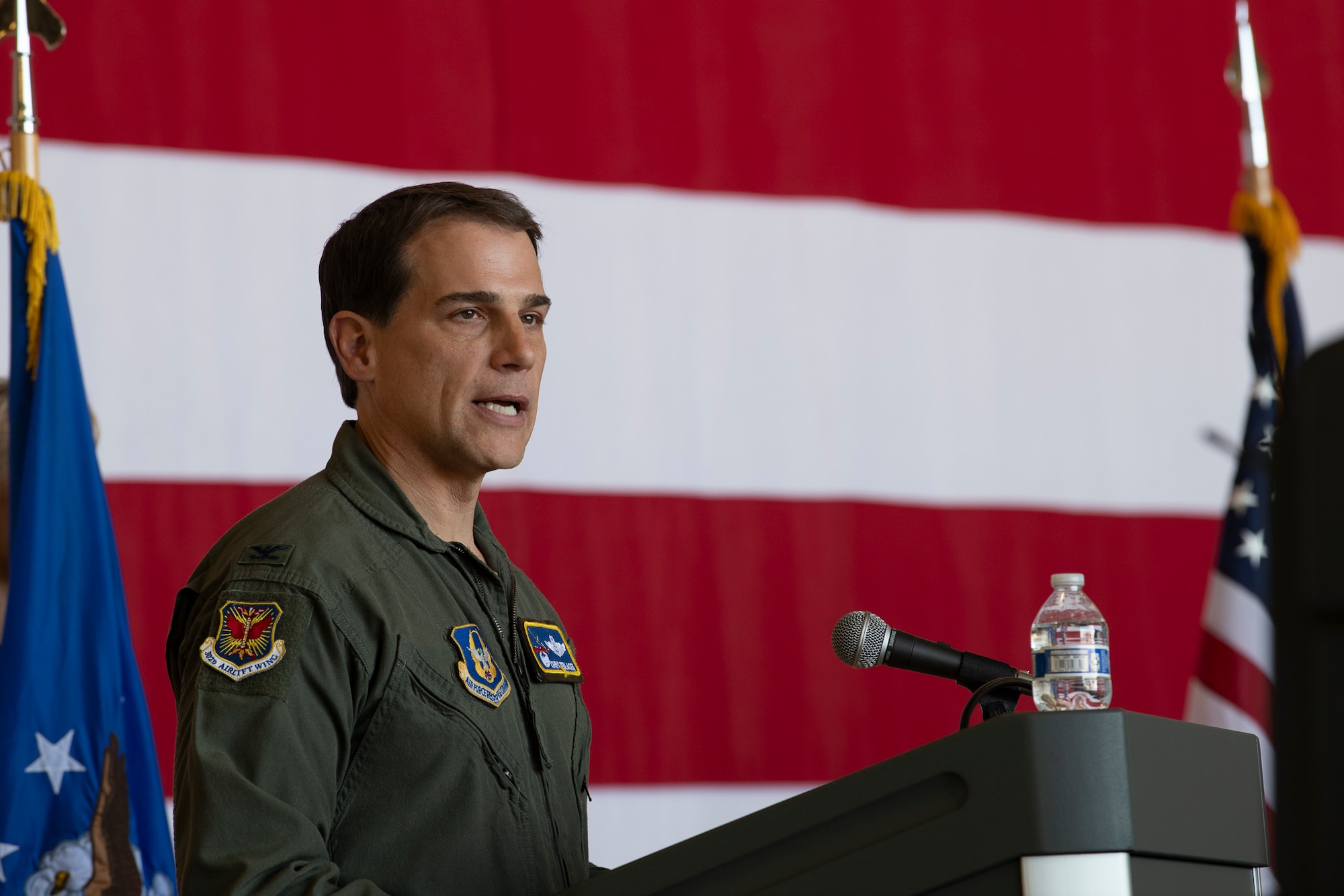 A man in a flight suit on stage in front of an American flag.