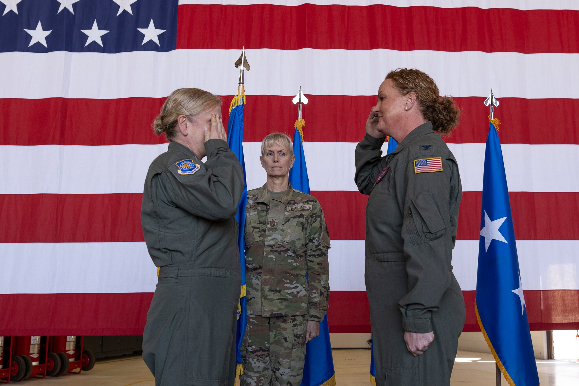 Two women saluting one another in front of an American flag on stage.