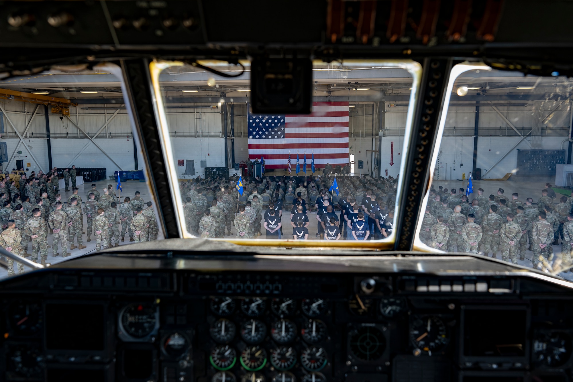 A military formation in front of a stage from inside the crew compartment of an aircraft.