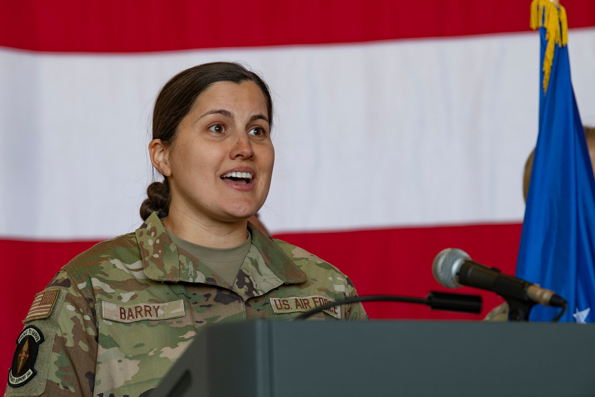 A woman in uniform sings on a stage in front of an American flag.