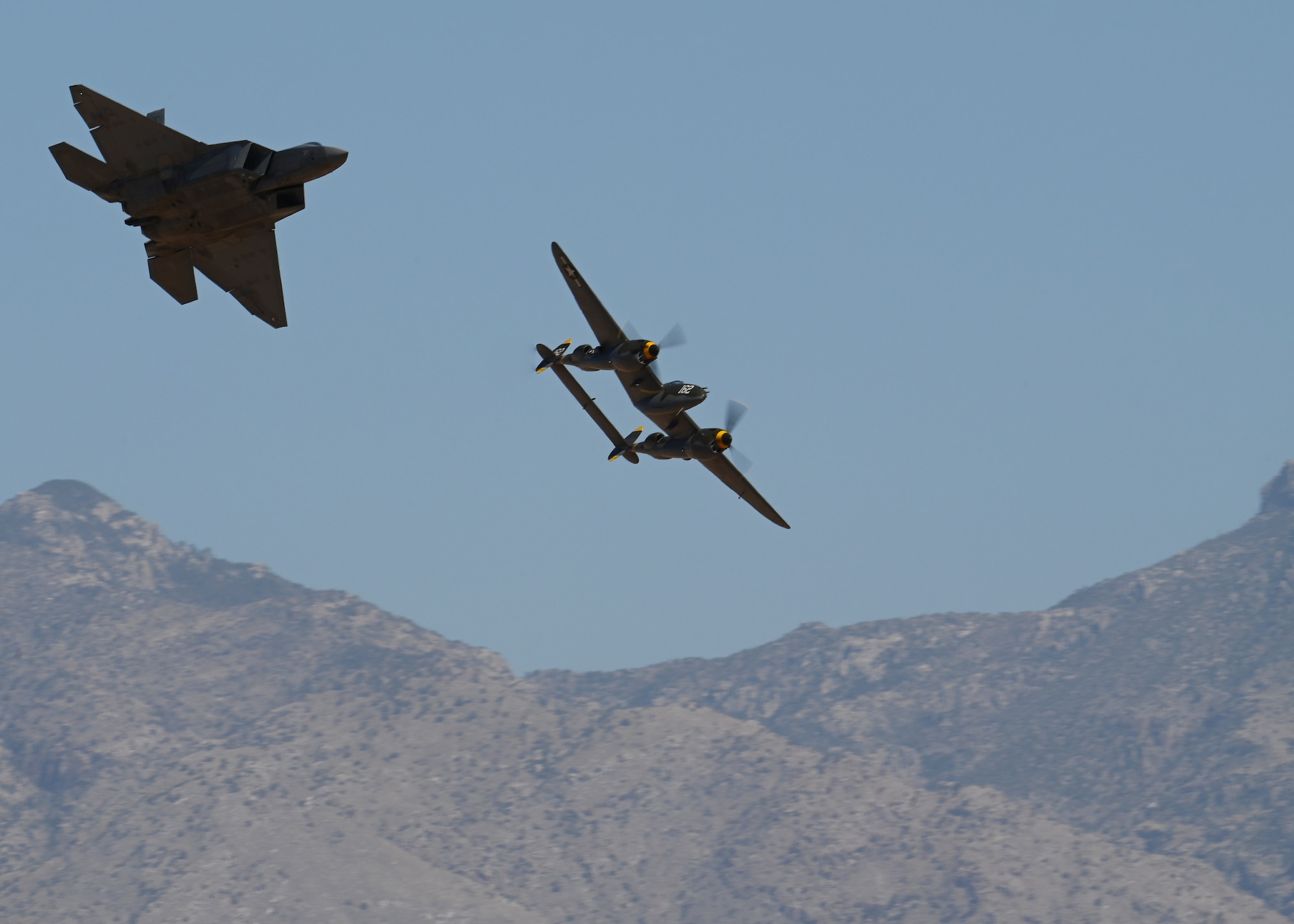 A U.S. Air Force F-22 Raptor aircraft, left, and the P-38 Lightning aircraft, right, fly during the Heritage Flight Training Course at Davis-Monthan Air Force Base, Arizona, March 2, 2025. The HFTC demonstrates the evolution of the United States’ Air Power. (U.S. Air Force photo by Staff Sgt. Abbey Rieves)