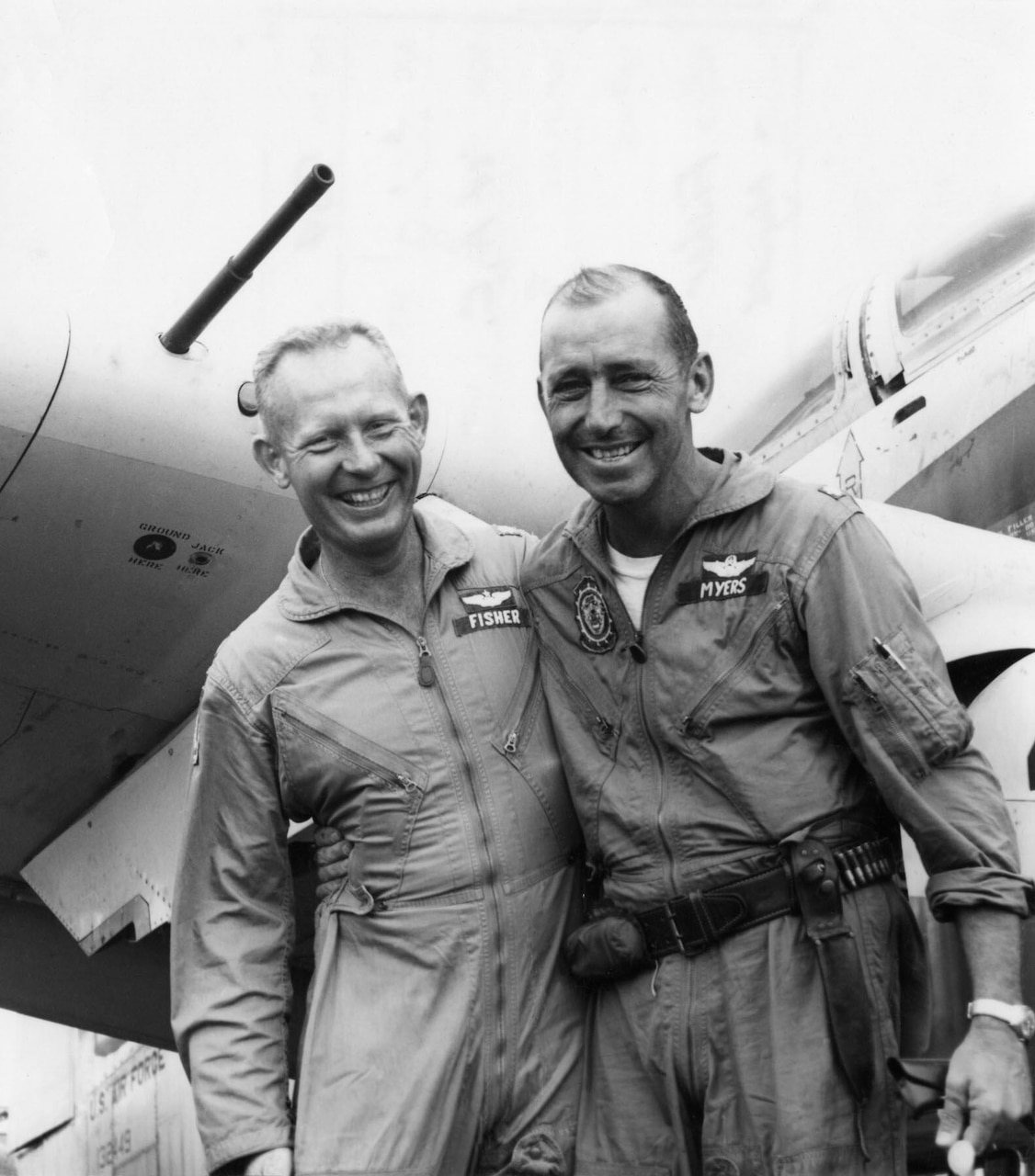 Two men give each other a side hug in front of an airplane.