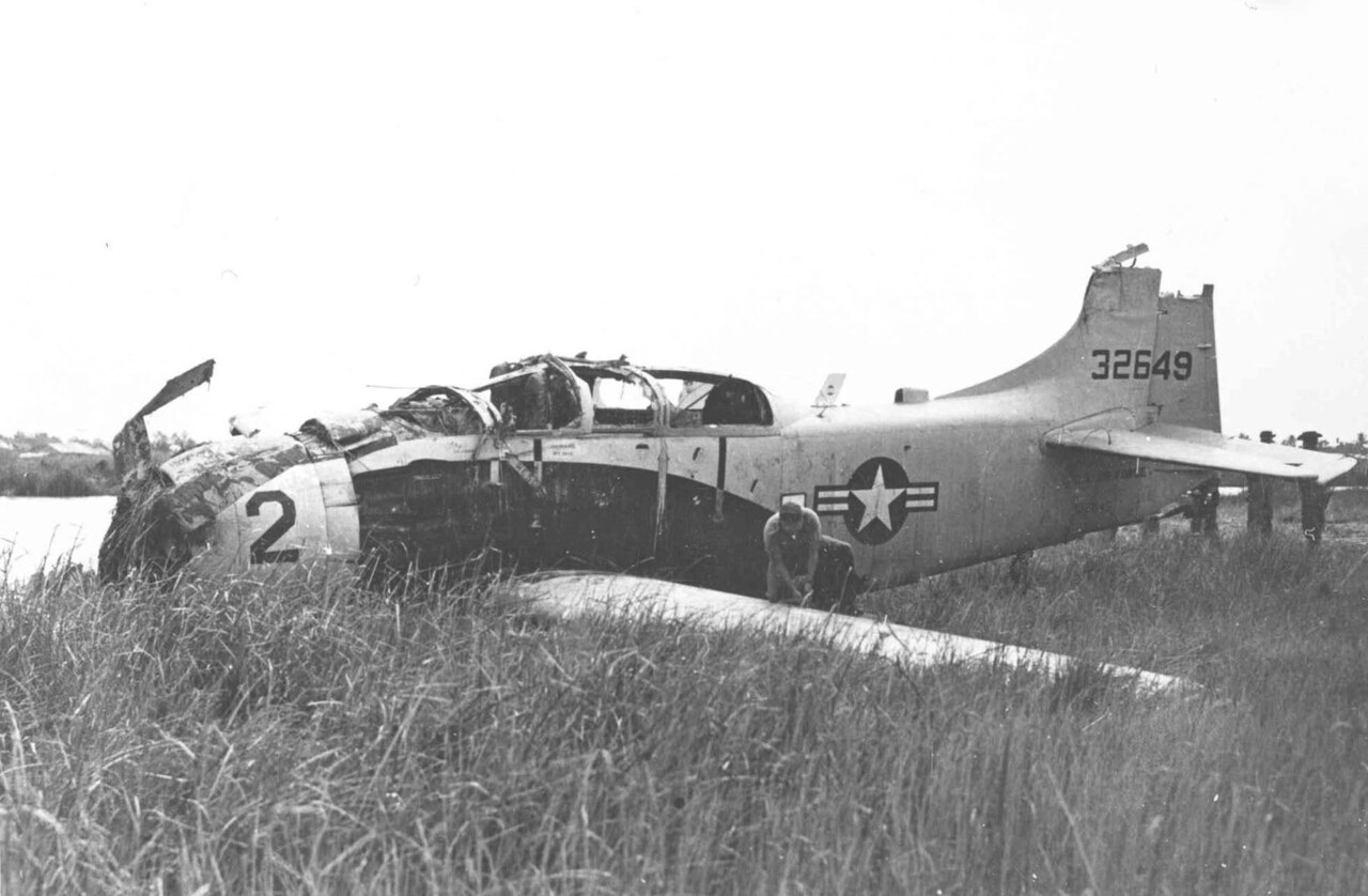 A damaged propeller airplane sits in tall grass.