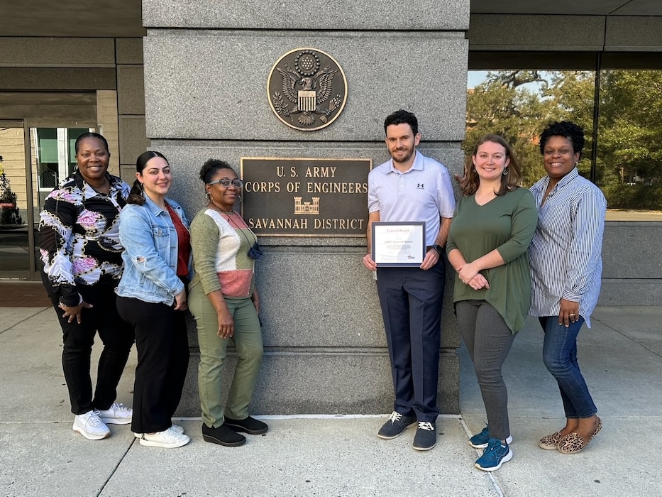 Six people standing in front of USACE Savannah District sign, holding an award.