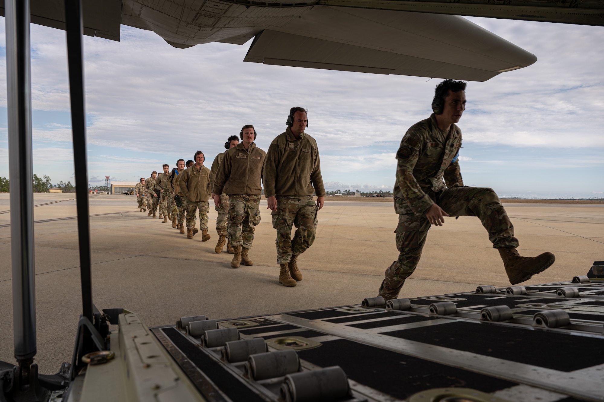 A line of U.S. Airmen are stepping on a C-130 ramp.
