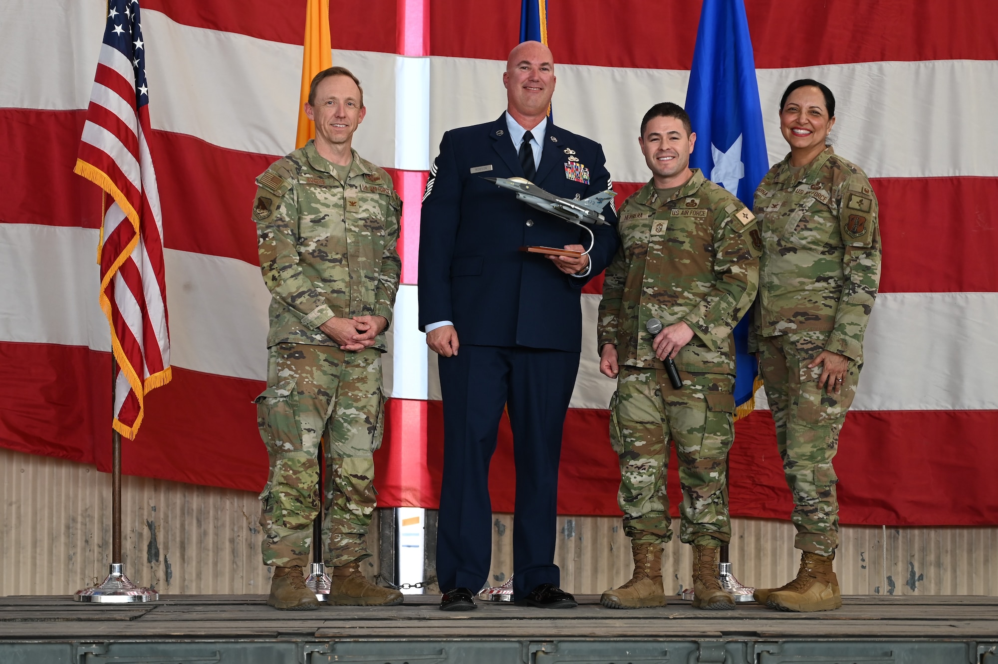 Four military members in uniform on stage during a ceremony.
