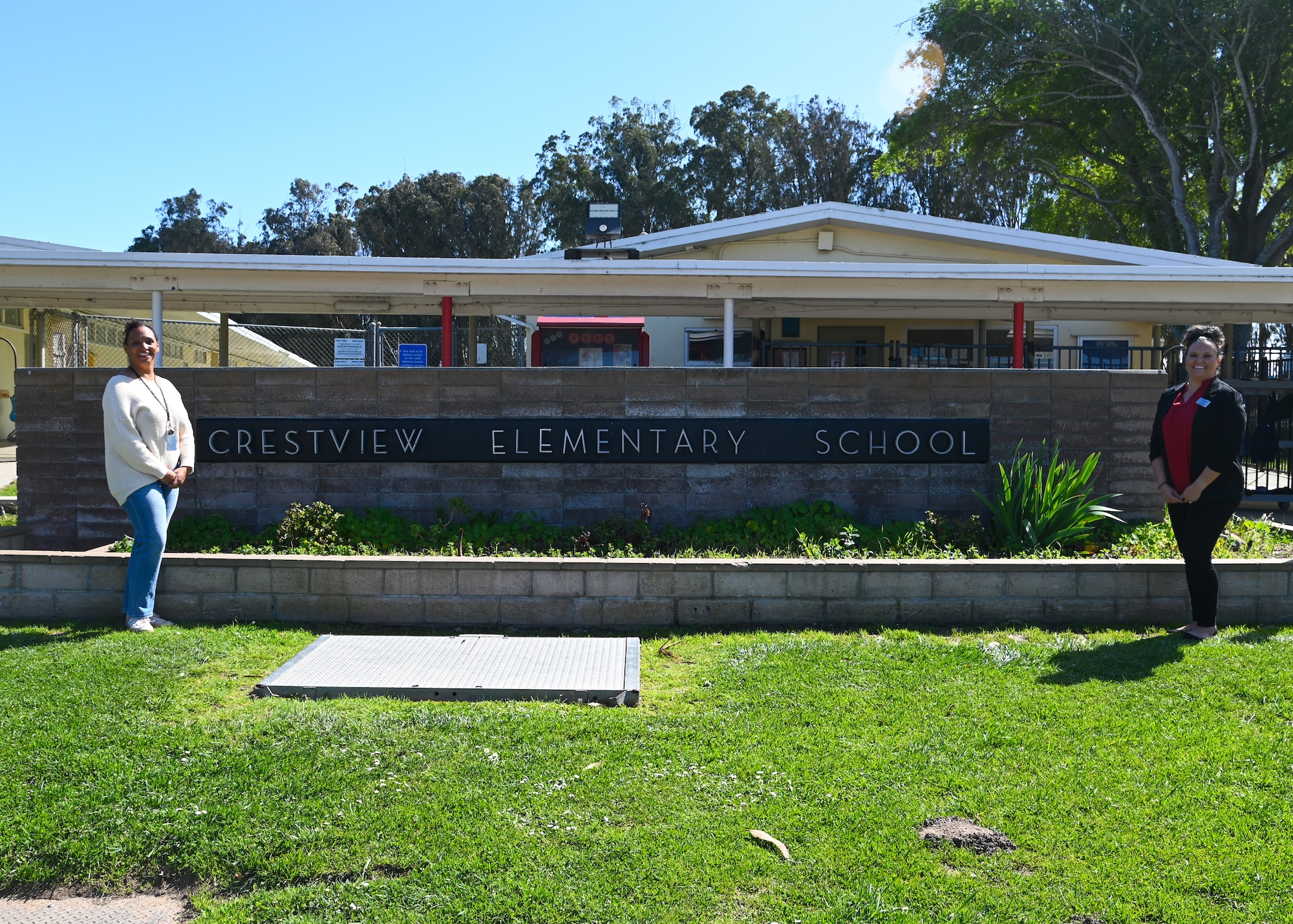 two women stand in front of a sign that says crestview elementary school outside of the school