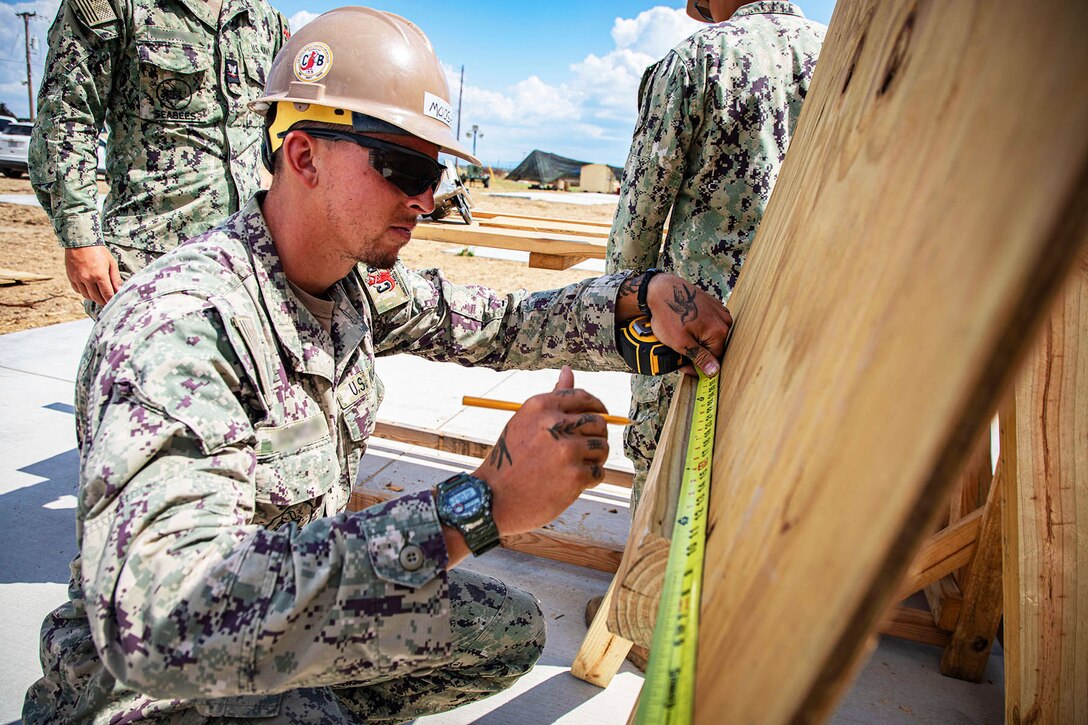 A sailor uses a measuring tape on a piece of wood.